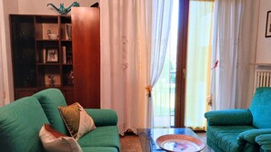 A living room with a green sofa, a glass coffee table, and a bookshelf. - CN040 ​​- Cesenatico, four-room apartment with balcony and parking, 30 meters from the sea. (Cesenatico)