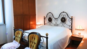A bed with a metal frame, two upholstered chairs, a bedside table with a lamp, and a window with curtains. - CN040 ​​- Cesenatico, four-room apartment with balcony and parking, 30 meters from the sea. (Cesenatico)