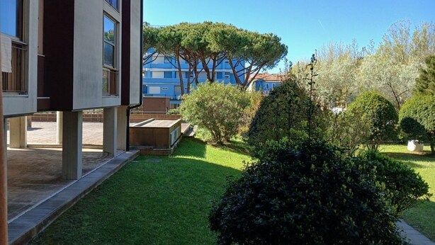 A courtyard with a building, a tree, and a well-maintained lawn. - CN040 ​​- Cesenatico, four-room apartment with balcony and parking, 30 meters from the sea. (Cesenatico)