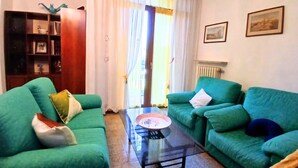 A living room with two green sofas, a glass coffee table, a bookshelf, and a door with curtains. - CN040 ​​- Cesenatico, four-room apartment with balcony and parking, 30 meters from the sea. (Cesenatico)