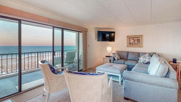 Een balkon met uitzicht op het strand, een bank, een stoel en een aan de muur bevestigde televisie.