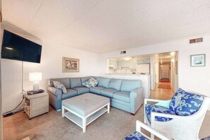 Ein Wohnzimmer mit einem Ecksofa, einem weißen Sessel, einem kleinen Tisch und einem Fernseher.