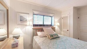 Een slaapkamer met een bed, nachtlampjes, een raam met zonwering, een deur en een spiegel.