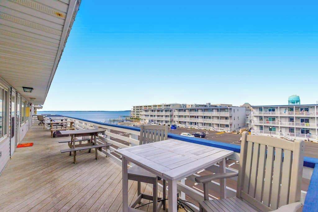 A balcony with wooden furniture overlooking a beach and a hotel building.