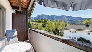 Un balcón con una mesa, sillas y vistas a un paisaje montañoso.