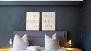 Un dormitorio con cama, almohadas, mesitas de noche y dos letreros en la pared.
