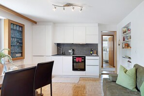 Una cocina moderna con armarios blancos, horno empotrado y comedor con mesa y sillas.