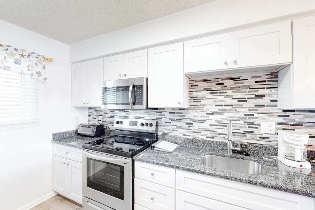 A modern kitchen with white cabinets, a stainless steel oven, a microwave, a gas stove, a sink, and a coffee maker.