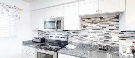 A modern kitchen with white cabinets, a stainless steel oven, a microwave, a gas stove, a sink, and a coffee maker.