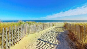 Ein Sandweg am Strand, an einer Seite eine Holzlattenzaun und auf der anderen Seite das Meer.