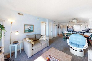 A living room with a sofa, a chair, a table, and a lamp. There is a painting on the wall and a door leading to another room. - Blaire Isle 301 S (Ocean City)