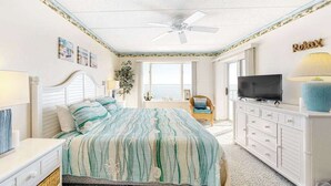 Een slaapkamer met een bed, een televisie, een plafondventilator en uitzicht op zee.