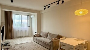 A modern living room with a sofa, a dining table with chairs, a TV, and a lamp. - Cozy minimalistic apartment in Bagebi (T'bilisi)
