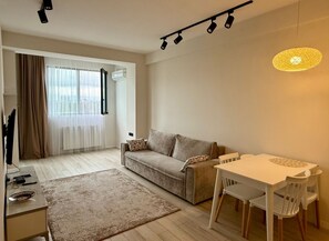 A modern living room with a sofa, a dining table with chairs, a TV, and a lamp. - Cozy minimalistic apartment in Bagebi (T'bilisi)
