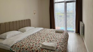 A bedroom with a bed, a radiator, a window with curtains, and a view of a balcony. - Cozy minimalistic apartment in Bagebi (T'bilisi)