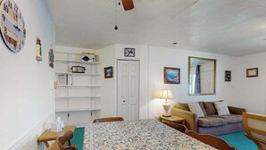Une pièce comprenant un lit, un canapé, une table et une chaise. Il y a une horloge au mur et une porte à l’arrière-plan.