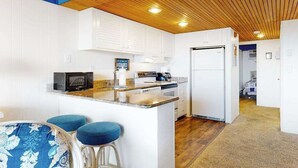 Une cuisine compacte avec des meubles blancs, un four à micro-ondes, une cuisinière et un réfrigérateur. On y trouve également un petit îlot avec des tabourets.