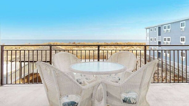 Un balcon avec des meubles en osier, une vue sur la plage et un bâtiment en arrière-plan.
