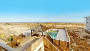 Une terrasse en bois avec une piscine, donnant sur une plage.
