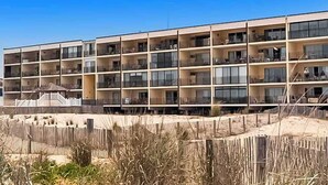 Un hôtel à plusieurs étages doté de balcons, une plage de sable en premier plan et un ciel bleu dégagé.