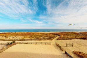 Ein Strand mit einem sandigen Pfad, der zum Meer führt, einem Holzzaun und einem klaren Himmel.