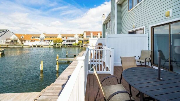 A waterfront deck with a table and chairs, a white fence, and a view of houses across the water. - Canal View Townhouse w/Private Deck, Washer/Dryer, & Private Balcony (Ocean City)