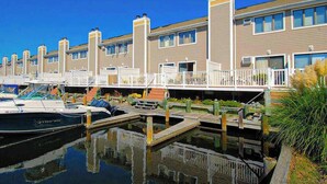 A marina with docked boats, a waterfront building with balconies, and a clear blue sky. - Canal View Townhouse w/Private Deck, Washer/Dryer, & Private Balcony (Ocean City)