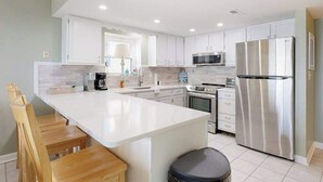 Una cocina moderna con armarios blancos, electrodomésticos de acero inoxidable y una isla central con asientos.
