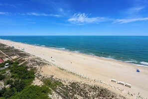 Een strand met een zandstrand, een heldere blauwe lucht en enkele gebouwen langs de kustlijn.