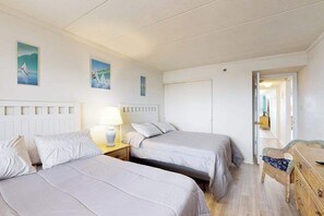 A bedroom with two beds, a nightstand, a dresser, and a door leading to another room. - Breezy Beachfront Condo w/Balcony, A/C and Fast WiFi (Ocean City)