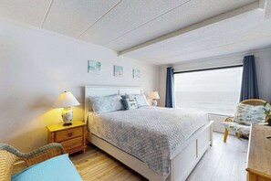 Een slaapkamer met een bed, nachtkastjes, een stoel en een raam met gordijnen.