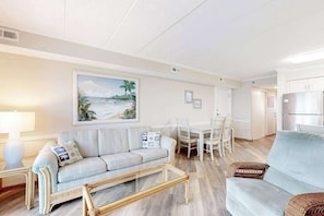 A living room with a sofa, a coffee table, a dining table with chairs, and a kitchen area with cabinets. - Marigot Beach 1206 (Ocean City)