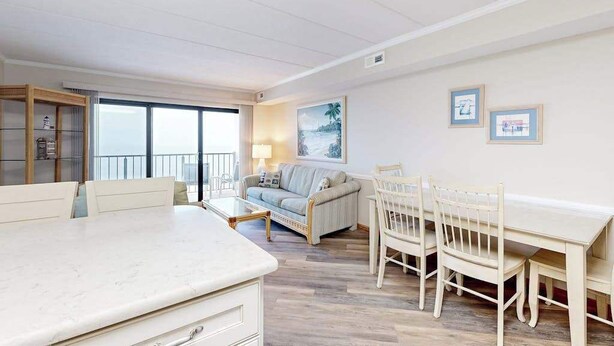 A room with a dining table, chairs, a sofa, and a window with a view. - Marigot Beach 1206 (Ocean City)