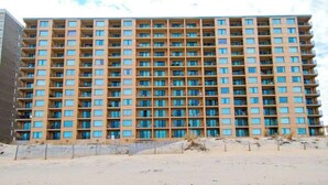 A high-rise building with multiple floors, balconies, and a sandy ground in front. - Marigot Beach 1206 (Ocean City)