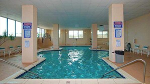 An indoor swimming pool with clear water, surrounded by beige pillars, and equipped with safety signs. - Marigot Beach 1206 (Ocean City)