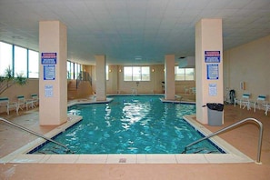An indoor swimming pool with clear water, surrounded by beige pillars, and equipped with safety signs. - Marigot Beach 1206 (Ocean City)