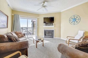 Ein Wohnzimmer mit Sofa, Sessel, Kamin, Fernseher und Deckenventilator.