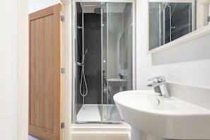 A modern bathroom with a glass-enclosed shower, a wooden door, and a white sink. - Old Dutch Embassy by Guestz (Hull)