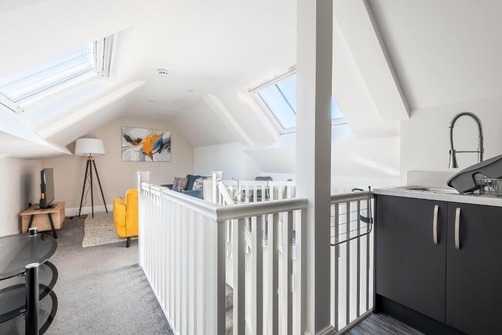 A loft-style room with a sloped ceiling, skylights, a dining area with a table and chairs, a kitchen with dark cabinets, and a white railing.