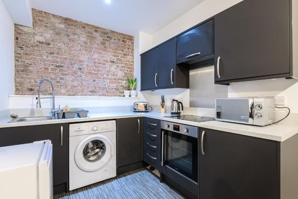 Une cuisine compacte équipée d’un lave-linge, d’un four, d’un four à micro-ondes et dotée d’un mur en briques.