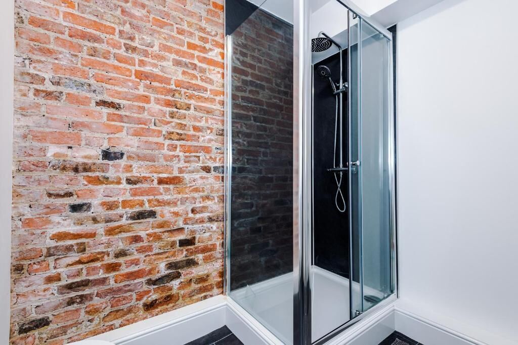Een kamer met een bakstenen muur, een douchecabine van glas en een witte vloer.