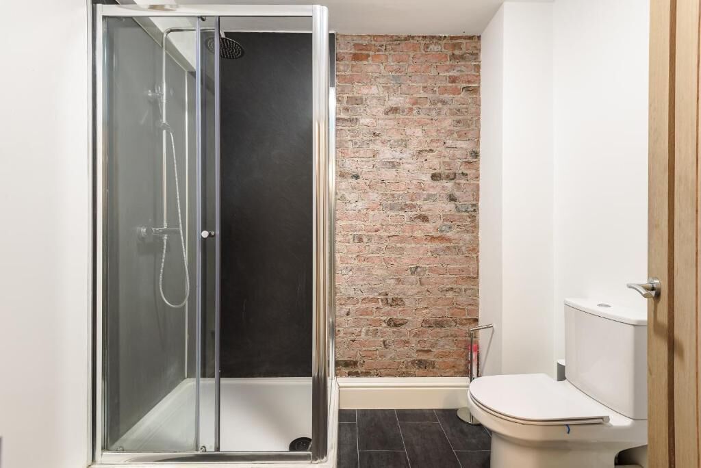 A bathroom with a glass-enclosed shower, a brick wall, and a white toilet.