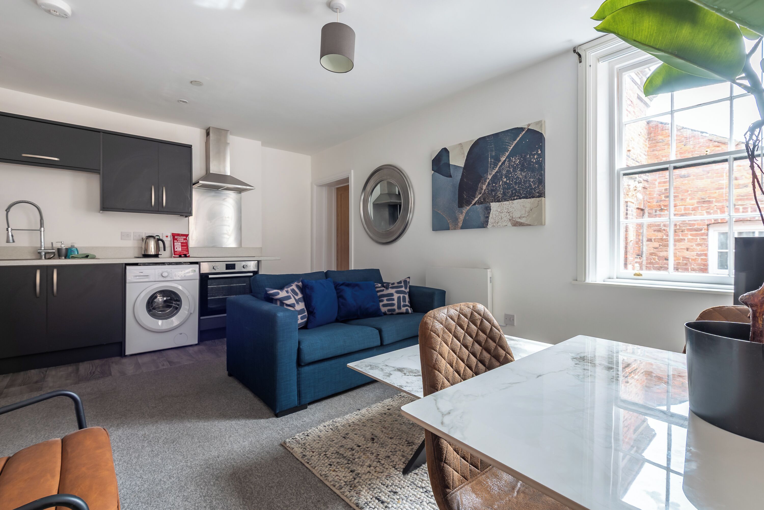 A modern kitchen with dark cabinets, a washing machine, and a blue sofa.