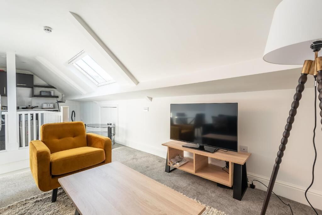 Un salon moderne avec un canapé, une table basse, un téléviseur posé sur un meuble et une lampe.
