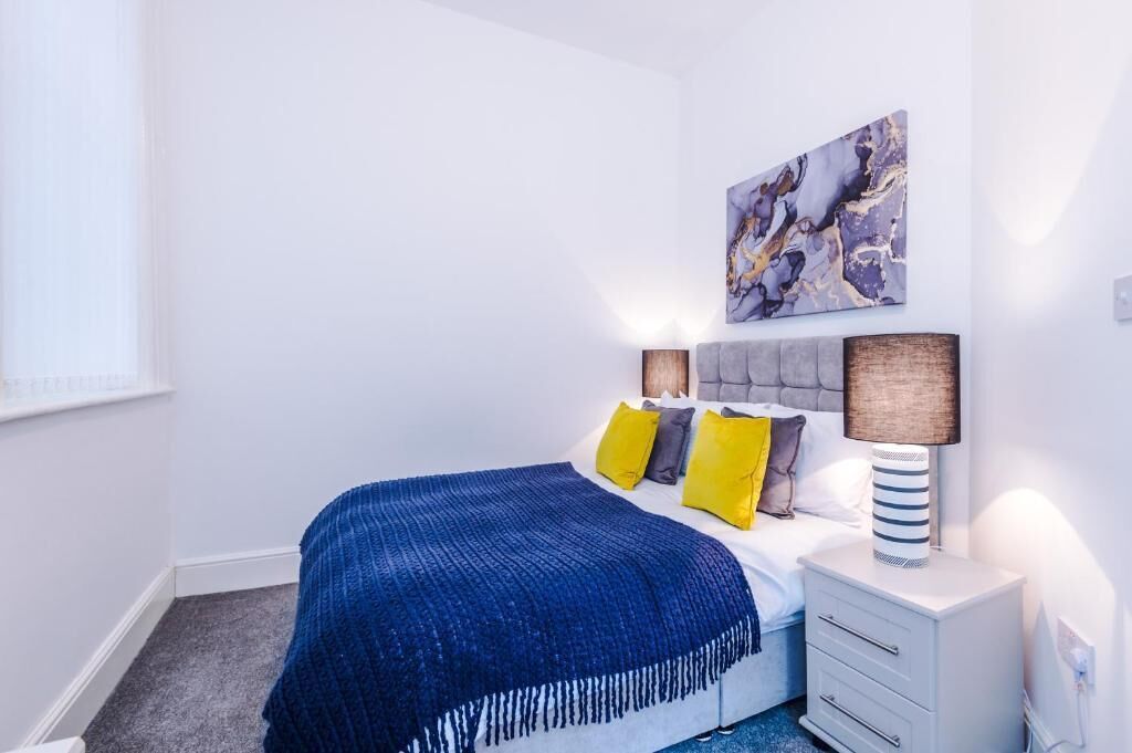 Een slaapkamer met een bed, nachtkastje, lamp en een wanddecoratie met abstracte kunst.