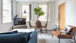 A living room with a sofa, a dining table with chairs, a TV, and a plant.