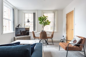 Een woonkamer met een bank, een eettafel met stoelen, een televisie en een plant.