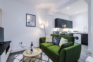 A modern living room with a green sofa, a round coffee table, and a flat-screen TV.