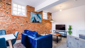 A living room with a brick wall, a blue sofa, a TV, and a table.