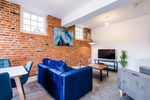 A living room with a brick wall, a blue sofa, a TV, and a table. - Old Dutch Embassy by Guestz (Hull)